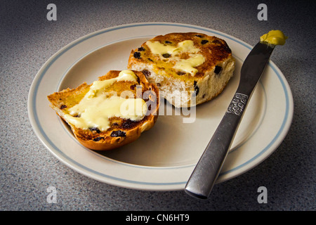 Hot Cross Buns am Karfreitag, getoastet und mit Butter auf einem Teller Stockfoto