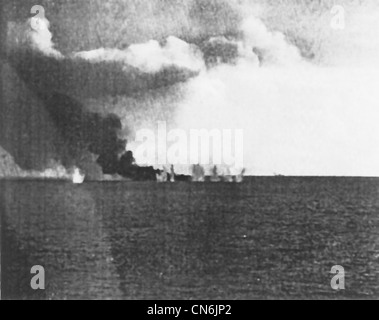 Eine 8-Zoll-Salve von entweder japanischen Kreuzer Tone oder Chikuma streckt sich die brennende US-Escort-Carrier Gambier Bay am 25. Oktober 1944 während der Schlacht vor Samar. Der japanische Kreuzer ist in der Mitte rechts auf dem Foto schwach zu sehen. Stockfoto