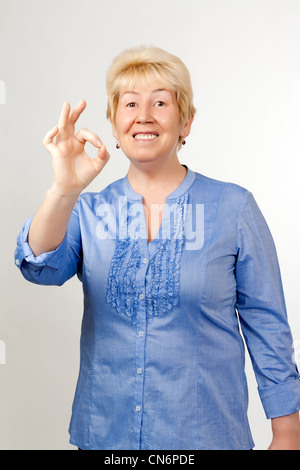 Frau mittleren Alters zeigt "OK", auf graue dackground Stockfoto