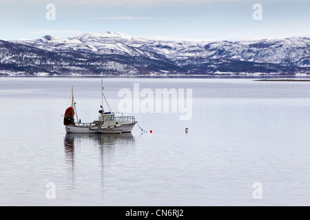 Ein Boot vor Anker in einem Fjord mit Schnee bedeckten Berge in der Ferne hinter Stockfoto