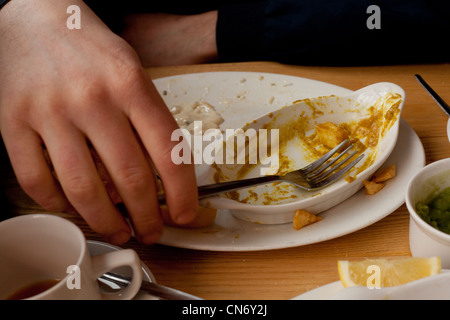 Ein Mann beendet einen Teller mit Fish &amp; Chips Erbsenpüree und Curry-Sauce in St. Ives, Cornwall Stockfoto