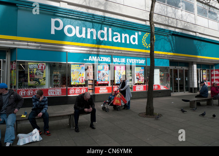 Eine Frau mit einem Kind in einem Kinderwagen und Menschen sitzen auf Bänken außerhalb Poundland Swansea, Wales, UK Stockfoto