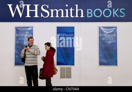 Ein paar steht vor einem großen Plakat für WHSmith Bücher, Stansted Flughafen Essex UK Stockfoto