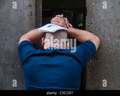 Ein Mann lehnt sich an einen schmalen offenen Tür abgewandten mit seinen Händen auf dem Kopf und Arme gegen die Wand in Havanna, Kuba. Stockfoto