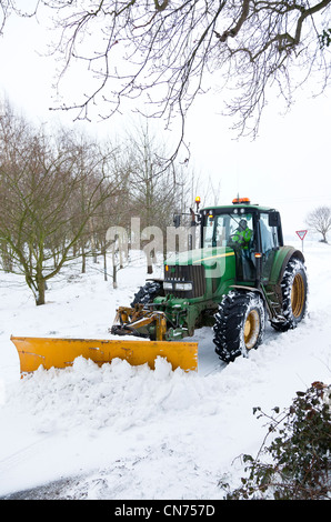 Ein Traktor mit einem Schneepflug, Schneeräumung von einer Landstraße montiert Stockfoto