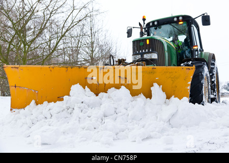 Ein Traktor mit einem montierten Schneepflug Schneeräumung von einer Landstraße Stockfoto