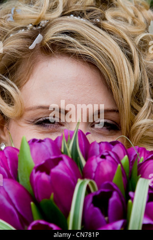 Eine junge Braut peeping über ihre violette Tulpen Strauß Stockfoto