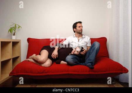 Junges Paar sitzt auf einem roten Sofa im Wohnzimmer Stockfoto