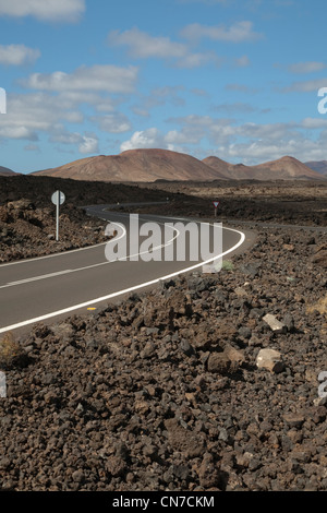 Straße durch die Lavafelder von Lanzarote auf den Kanarischen Inseln mit den Vulkanen des Timanfaya im Hintergrund Stockfoto