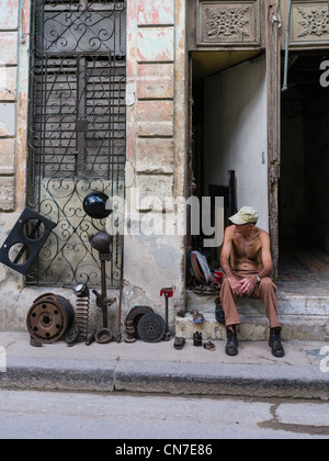 Ein Mann mittleren Alters kubanischen sitzt auf der vorderen Stoop seines Hauses Verkauf verwendet Autoteile in Havanna, Kuba. Stockfoto