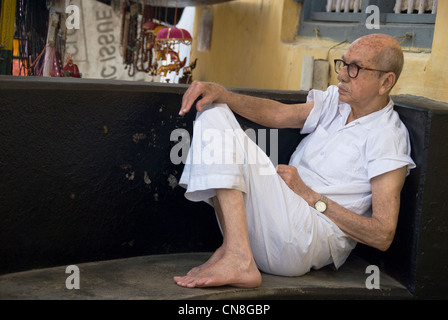 Älterer Mann sitzt auf der Veranda seines Hauses. Szene aus Jude Street, Mattancherry, Cochin, Kerala. Stockfoto