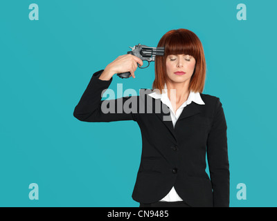 Porträt von einem aggressiven, schöne, junge Geschäftsfrau, mit eine Pistole an den Kopf, auf blauem Hintergrund Stockfoto