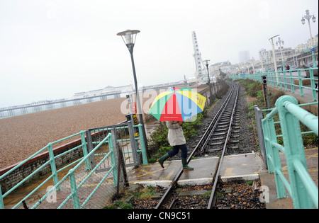 Frau mit einem hellen farbigen Dach zu Fuß über Volks Railway tracks auf einem nassen Ostern Wochenende und Feiertagen Stockfoto