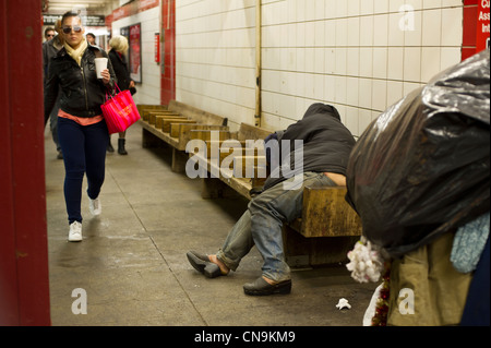 Ein Obdachloser schläft auf einer Bank im u-Bahnhof 5th Avenue in Midtown in New York Stockfoto