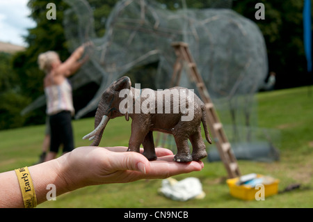 Nahaufnahme einer weiblichen Hand, die Spielzeug-Elefanten hält, um lebensgroße Drahtelefanten beim Port Eliot Literaturfestival St. German Cornwall zu modellieren Stockfoto