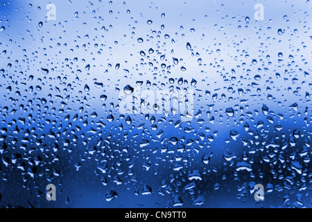 Eine Nahaufnahme von blauen Wassertropfen auf einer Glasscheibe Fenster. Stockfoto