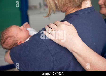 Eine Krankenschwester legt eine tröstende Hand auf eine Mütter-Schulter, wie sie hier neugeborenes Baby UK wiegen Stockfoto