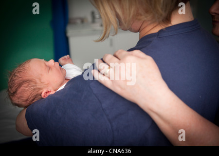 Eine Krankenschwester legt eine tröstende Hand auf eine Mütter-Schulter, wie sie hier neugeborenes Baby UK wiegen Stockfoto