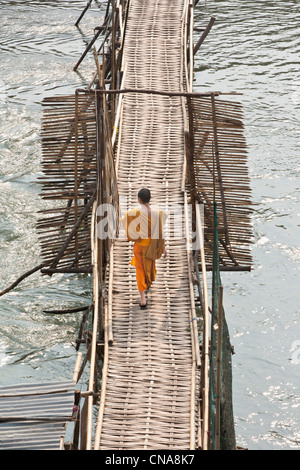 Ein junger buddhistischer Mönch zu Fuß über eine Bambusbrücke in Luang Prabang, Laos Stockfoto