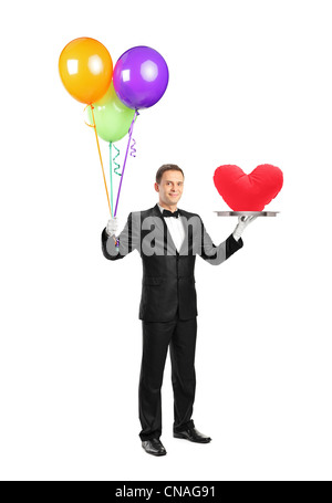 In voller Länge Portrait von einem Butler hält ein Tablett mit einer roten Herzform drauf und Ballons isoliert auf weißem Hintergrund Stockfoto