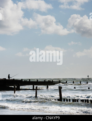 Einsamen Fischer am Strand von West Wittering mit Buhnen (Meer Verteidigung gegen Erosion) während einer Springflut high Stockfoto