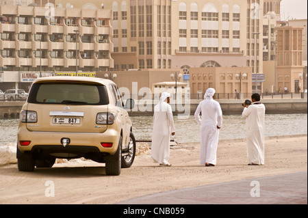 Drei Männer in Tracht mit ihrem Nissan Patrol 4WD Auto fotografieren am Dubai Creek, Vereinigte Arabische Emirate Stockfoto