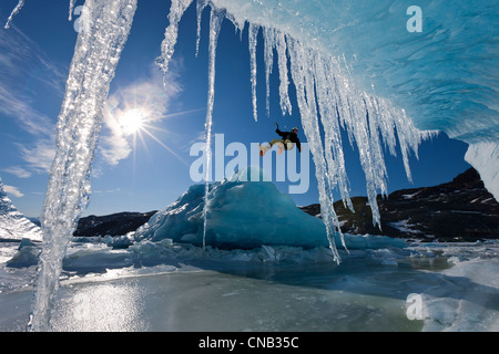 Zusammensetzung: Sonne scheint durch Eiszapfen hängen an einem Eisberg als ein Eiskletterer Abseilen über den Rand, Mendenhall Alaska Stockfoto