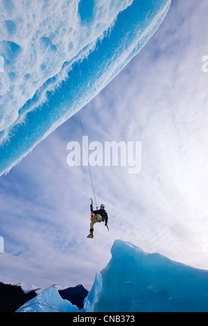 Ein Eiskletterer schwingt nach unten vom Seil zu Gesicht eines großen Eisbergs eingefroren in Mendenhall Lake, Juneau, Alaska, Winter Stockfoto