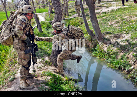 Soldat der US Army springt über einen Bewässerungskanal, unterstützt durch einen Kameraden während Patrouille 30. März 2012 in der Nähe des Dorfes von Gor Stockfoto