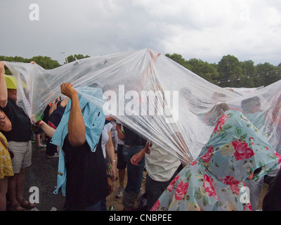 Eine Menschenmenge, die Zuflucht vor dem Regen unter ein Blatt aus Kunststoff bei einem Konzert im freien Stockfoto