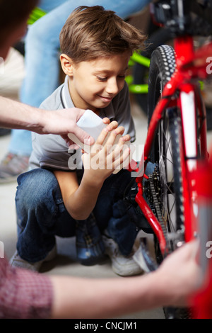 Porträt des netten jungen Schmieren der Fahrradkette in garage Stockfoto