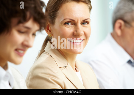 Lächelnde Geschäftsfrau, Blick in die Kamera bei ihren Partnern Stockfoto