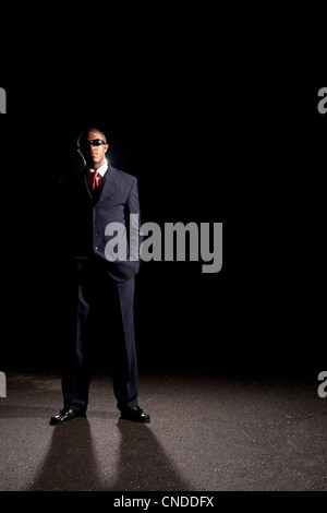 Ein afrikanischer amerikanischer Mann gekleidet in einem dunklen farbigen Anzug und Sonnenbrille steht man vor einem dunklen schwarzen Hintergrund. Stockfoto