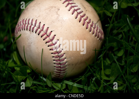 Nahaufnahme eines alten und abgenutzten Hardball oder Baseball im grünen Gras. Geringe Schärfentiefe. Stockfoto