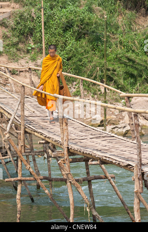 Ein junger Mönch geht über eine Bambusbrücke in Luang Prabang Laos Stockfoto