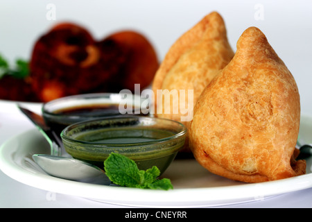 Beliebte indische, asiatische und afrikanische tief gebraten Snack genannt Samosa mit würzigen Chutney und Minze Stockfoto