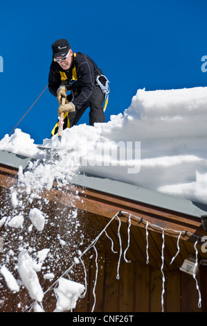 Mann, die Beseitigung von Schnee von einem Dach mit einem shovel.on einen sonnigen Tag Stockfoto