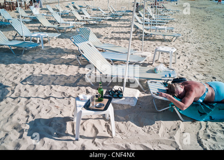 Eine Frau liegt auf einer Recling Sonnenliege am Strand in Griechenland auf der Insel Naxos. Stockfoto