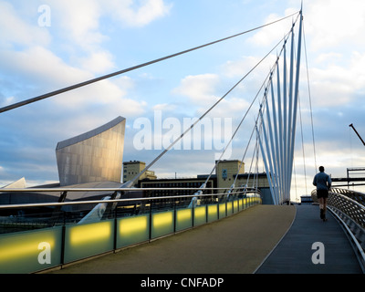 Die Medienstadt Fußgängerbrücke über den Manchester Ship Canal mit Imperial War Museum North im Hintergrund - Läufer auf Brücke Stockfoto