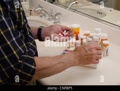 Älterer Mann, die Vorbereitungen für eine Hand voll von verschreibungspflichtigen Pillen mit Pille Flaschen im Hintergrund Stockfoto