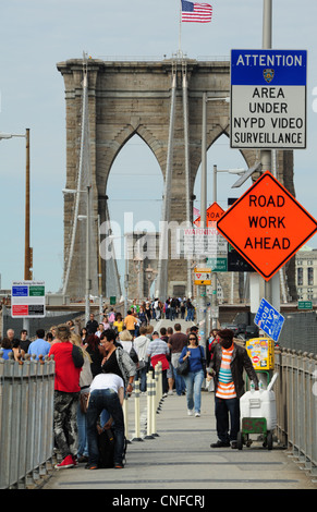 Menschen gehen, afrikanisch-amerikanischer Mann Wasser verkaufen, Turm amerikanische Flagge oben, Brooklyn Bridge Fußgängerweg, NewYork Stockfoto