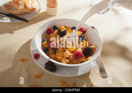 Milch gegossen wird, auf eine Schüssel Cornflakes mit Früchten Stockfoto