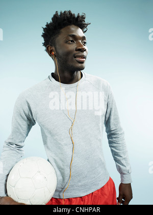 Ein junger Mann trägt Ohrstöpsel und hält einen Fußball Stockfoto