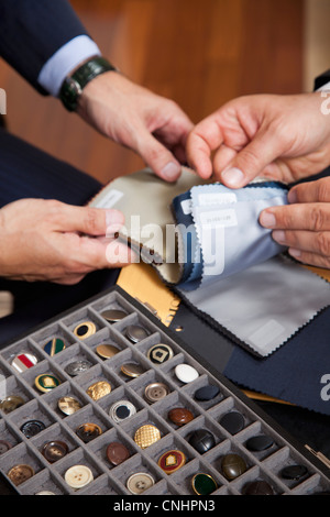 Detail eines Tabletts von Knöpfen und zwei Männer betrachten Stoffmuster Stockfoto