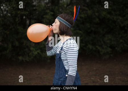 Junge Frau in Kopfschmuck, bläst einen Ballon Stockfoto