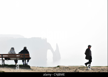 Ältere Touristen sitzen auf Bank, Blick auf die Porte D'Aval, natürlichen Bogen in Kreidefelsen bei Etretat, Haute-Normandie, Frankreich Stockfoto