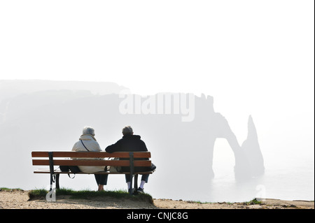 Ältere Touristen sitzen auf Bank, Blick auf die Porte D'Aval, natürlichen Bogen in Kreidefelsen bei Etretat, Haute-Normandie, Frankreich Stockfoto