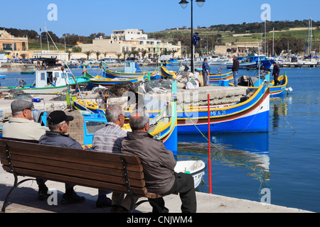 Gruppe von älteren Männern Ausschau über Angelboote/Fischerboote in Marsaxlokk Hafen, Malta, Europa Stockfoto