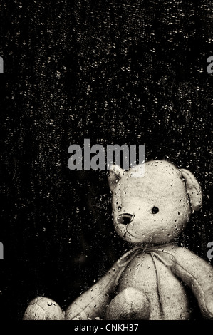 Traurig Teddybär durch ein Fenster in den regen Tropfen fallen. Sepia Getont. Noch immer leben Stockfoto
