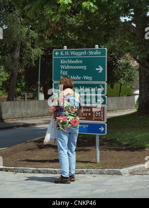 Eine weibliche Touristen starrte auf ein Straßenschild in Kirchboden für Wegbeschreibungen zu lokalen Sehenswürdigkeiten in Wargrain, in der Nähe von Salzburg Österreich. Stockfoto